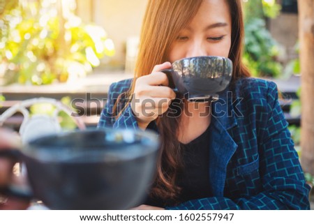 Close up image of a beautiful asian woman clinking and drinking coffee with friend in cafe