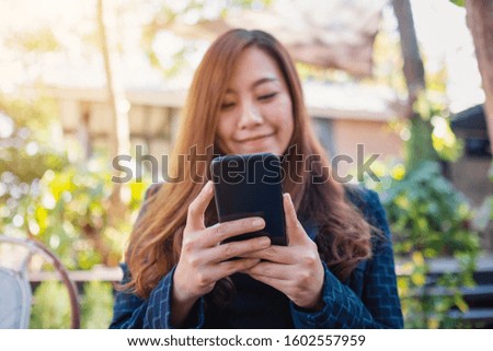 Closeup image of a woman holding , using and looking at mobile phone in the outdoors
