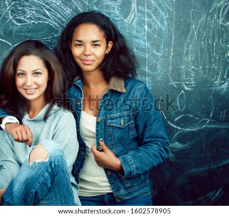 back to school after summer vacations, two teen real girls in classroom with blackboard painted together, lifestyle mixed races people concept