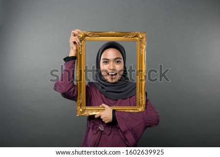 Portrait of  young woman full of emotions , holding picture frame isolated on background in studio. People sincere emotions, lifestyle concept