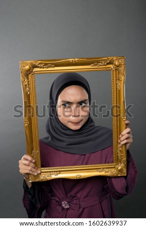 Portrait of  young woman full of emotions , holding picture frame isolated on background in studio. People sincere emotions, lifestyle concept