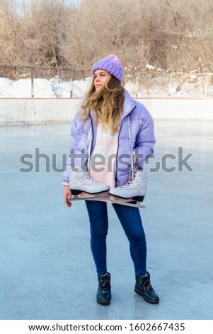 Lovely young woman with ice skates hanging on neck on the ice rink. Girl is going to skating on ice in a winter frosty day