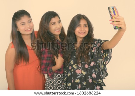 Three happy young Persian woman friends smiling while taking selfie picture with mobile phone togther against white background