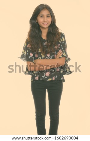Studio shot of young happy Persian woman smiling and standing with arms crossed isolated against white background