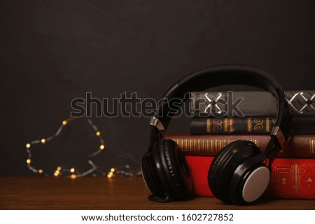 Books and headphones on wooden table against black background. Space for text