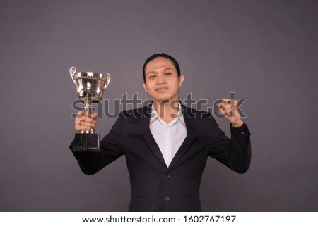 A young business man holding a gold trophy and celebrate his archivement.