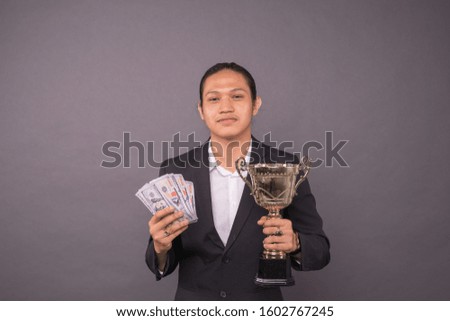 A young business man holding money and gold trophy.Successful achievement.