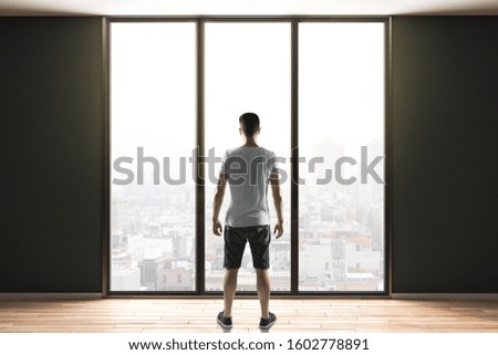 Young man in shorts standing in contemporary interior with panoramic city view.