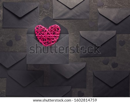 Romantic composition for Valentine's day. Red wicker heart is in a black envelope against a dark background. Decorating with paper black confetti in the form of hearts. Flat lay, copy space.