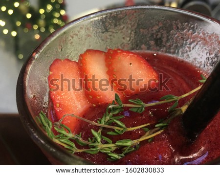 Close up picture of strawberry alice on top of a glass of red berry smoothie with green garniture decoration. Strawberry smoothie in a glass with a straw with a blurred background behind.