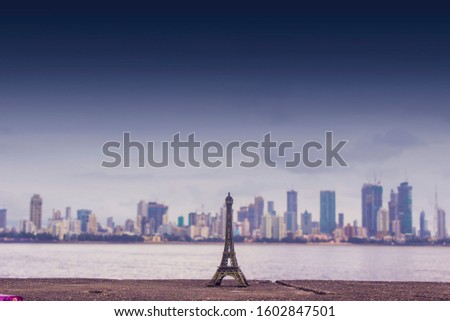 Replica of Eiffel Tower in front of a city scape skyline. Room for text and copy space. Eiffel tower miniature with dark clouds over landscape skyline in urban city.  