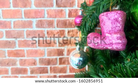 pink toy boot hanging on Christmas tree with red brick background