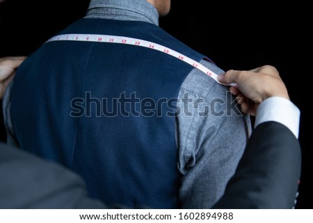 The dressmaker was measuring the width of the back of the man wearing a blue suit on black background. Royalty-Free Stock Photo #1602894988