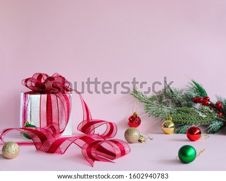 In the picture include: Gift box and Red bow, Pine tree branch, and many Colored balls in Pink background .