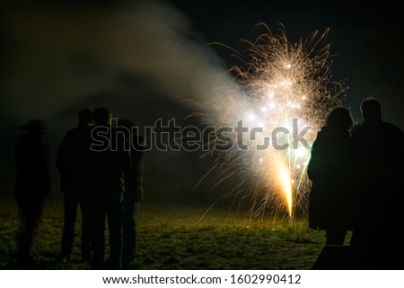 Friends stand together as silhouettes around a firework fountain to celebrate the new year at midnight, copy space