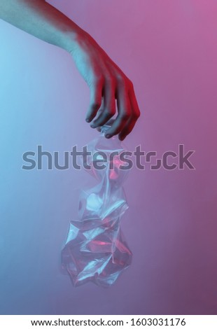Recycling concept. Female hand holds a rumpled plastic bottle. Creative pop art pink blue neon color. Trendy gradient illumination. Night light