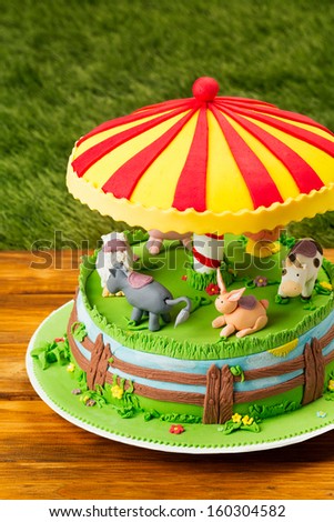 Fondant cake/Farm themed cake. Children cake on wooden table. Cake on picnic table on grass background. Holiday cake. Animal figures on cake. Carousel themed cake.
