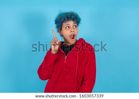 young african american woman isolated on blue background, with blue hair, with expression of creativity or imagination