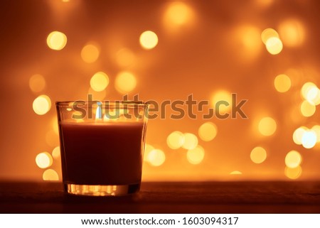 Silhouette of burning candle with golden blurred lights on dark background