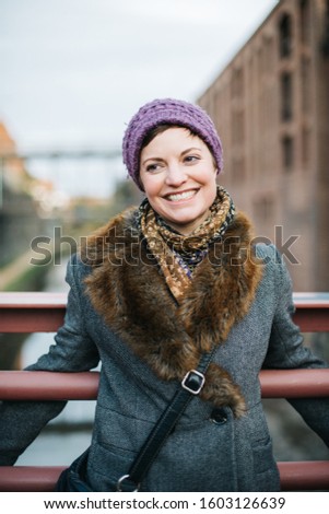 Smiling Caucasian woman portrait smiling and looking away, head and shoulders dressed in warm clothing wearing a knit hat and standing on a bridge over the canal in Georgetown, Washington DC. 