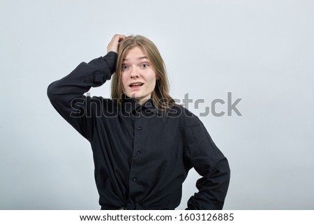 Disappointed young woman in fashion black shirt isolated on gray background in studio keeping hand on head and belt, confused. People sincere emotions, lifestyle concept.