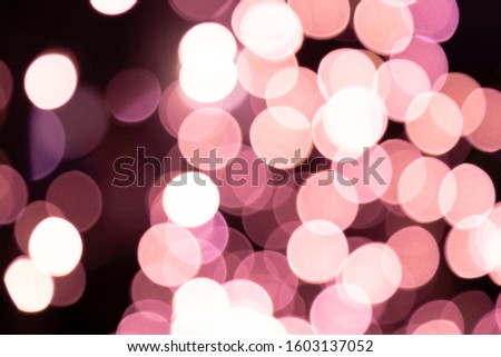 A picture of a multicolored bokeh light on a pedestrian street decorated on a tree from a lamp or car light. Using the camera lens makes the image blur beautiful in the natural black background.