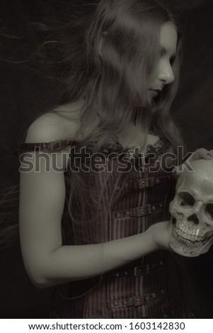 Gothic girl with skull posing over dark background