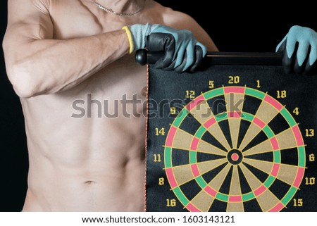A gloved man holds a dartboard against a dark background