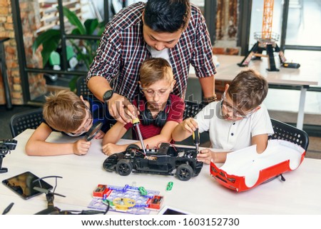 Male electronic engineer with european school children working in smart school lab and testing model of radio controlled electric car.