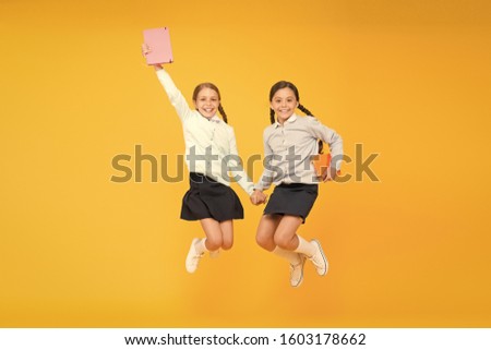 Passionate about books. Happy little girls jumping with books on yellow background. Cute small children smiling with encyclopedia or hand books. Educational books for pupils and students.