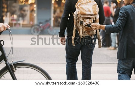 Thief stealing wallet from backpack of a man walking on street during daytime.  Pickpocketing on the street during daytime Royalty-Free Stock Photo #160328438
