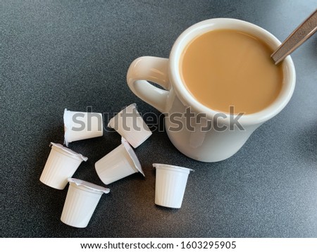 A cup of coffee with cream and single serving coffee creamer packages.