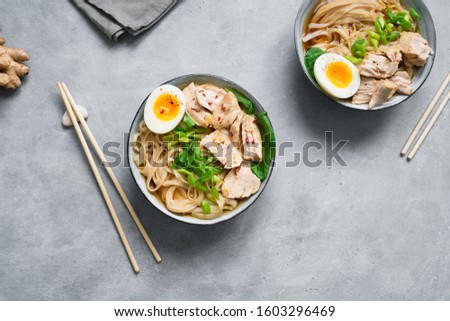 Asian ramen noodles soup with chicken, soft egg and greens on concrete background. Japanese food, ramen bowl for healthy lunch, copy space.