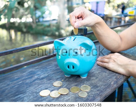 saving money into a blue piggy, many golden coins on the wooden