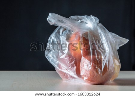 A plastic shopping bag is on a table. There are apples in the bag. Concept: environmentally harmful packaging