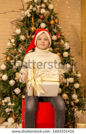 boy with a gift in his hands sits on a red barrel against the background of the Christmas tree