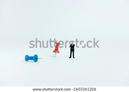 Miniature business concept - a businessman standing beside red and blue thumbtack / push pin with white background