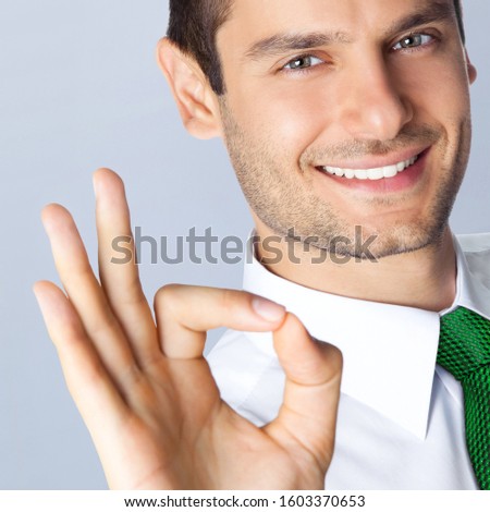 Portrait photo of confident businessman in green tie, showing okay gesture, isolated over grey background. Business concept picture. Square composition.
