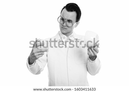 Studio shot of young crazy man doctor looking at piggy bank while holding empty coffee cup