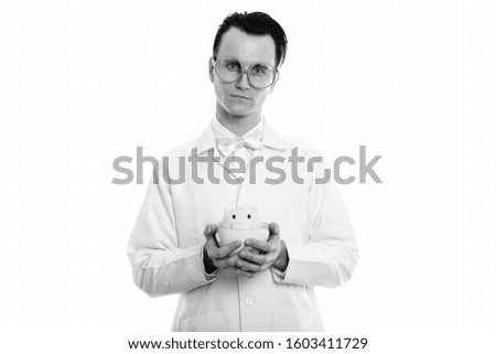 Studio shot of young crazy man doctor holding coffee cup with piggy bank inside