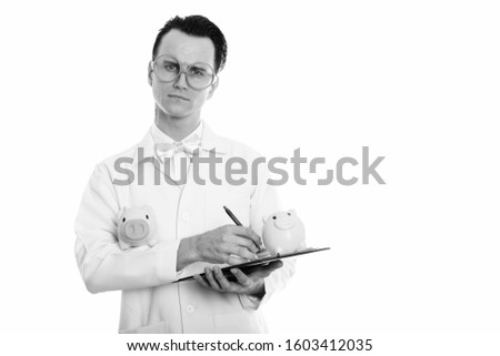Studio shot of young crazy man doctor writing on clipboard with two piggy banks on hand