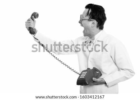 Profile view of young crazy man doctor holding and shouting at old telephone