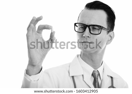 Studio shot of young handsome man doctor looking closely at vitamin tablet