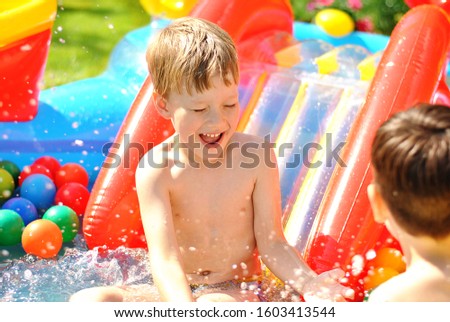 Laughing boy on the playground. Sunny summer mood picture. Cheerful kid playing in the swimming pool with water drops under the bright sunshines. Childish playful joy and happy childhood concept.