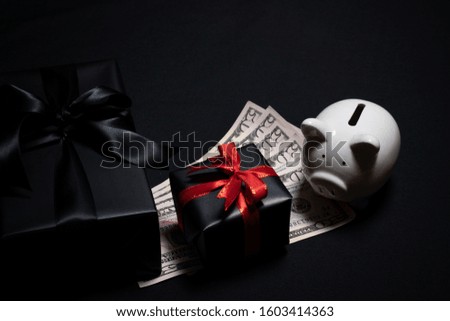 Top view of gift box with red, black ribbons, money and piggy bank isolated on black background. Shopping concept boxing day and black Friday sale composition.