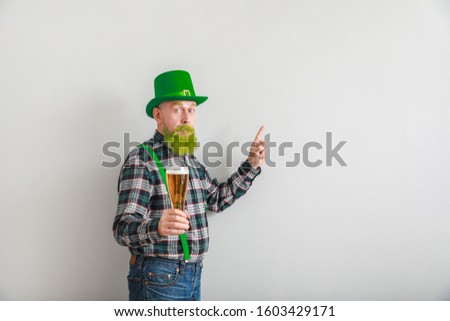 Funny mature man with glass of beer showing something on light background. St. Patrick's Day celebration
