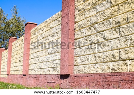Fence made of bricks and decorative plaster. Yellow fence with red elements. High and beautiful fencing.