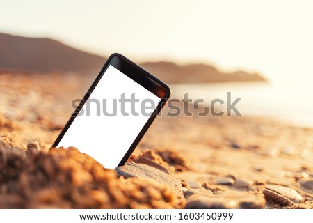 The concept of the photos on the phone. The smartphone lies buried in the sand on the beach, and takes a photo of the beach in the background. Mock up