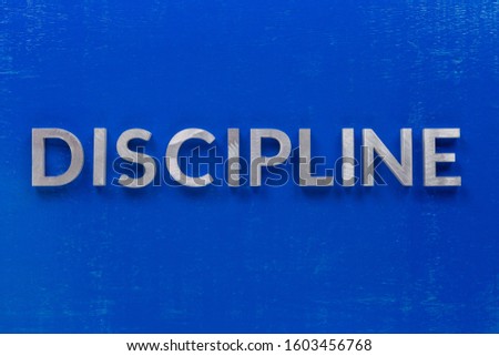 the word discipline laid with silver metal characters on blue painted wooden board in central flat lay composition