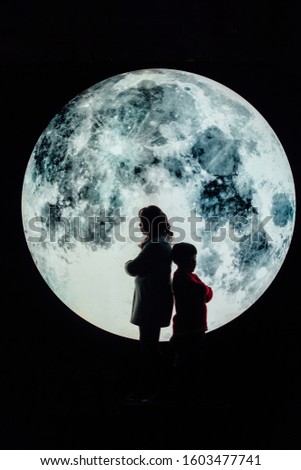 Silhouette picture of grandma and grandson stand on the mountain with A big full moon at night.